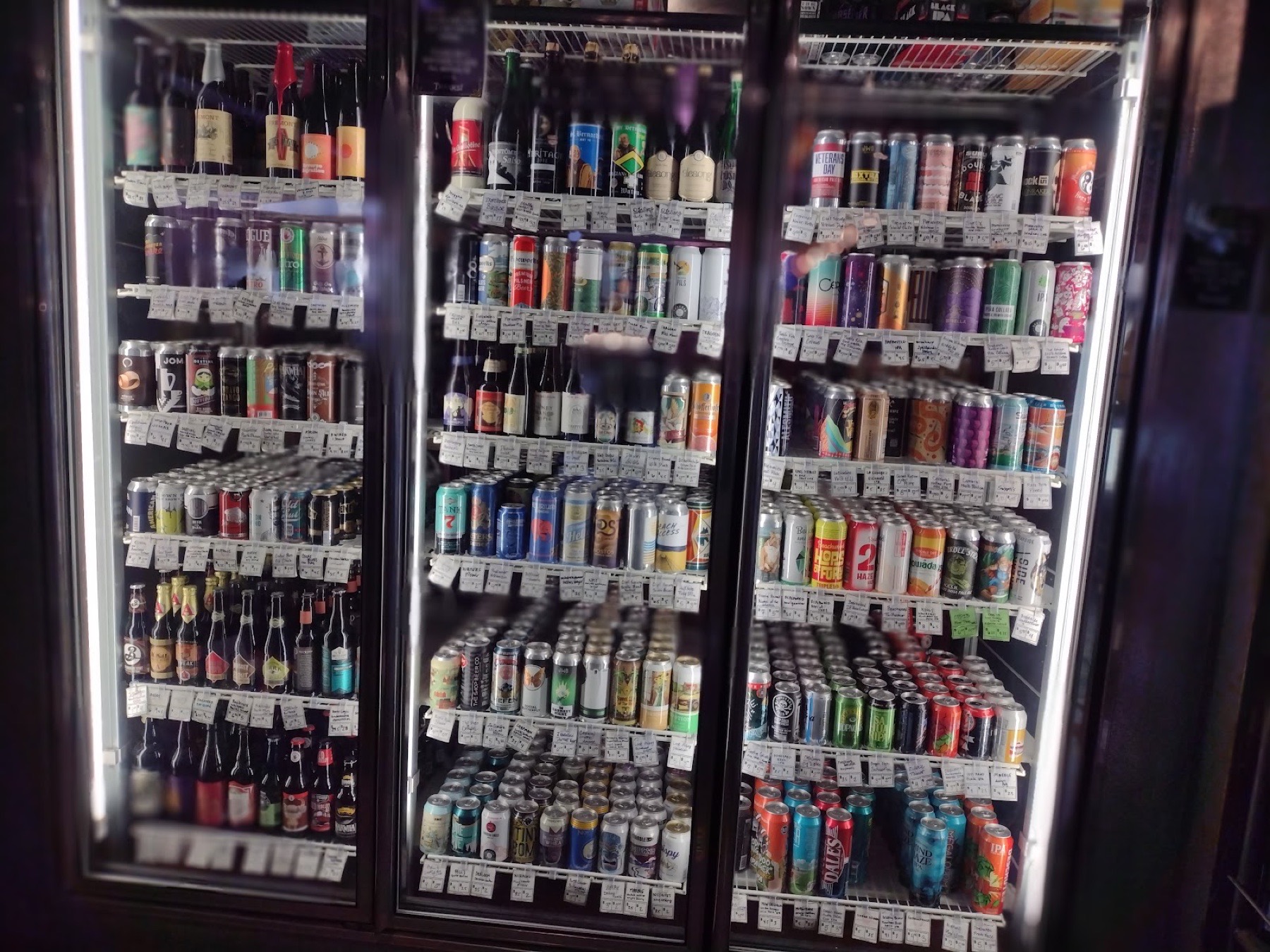 Three glass-door coolers packed with hundreds of craft beer cans and bottles.