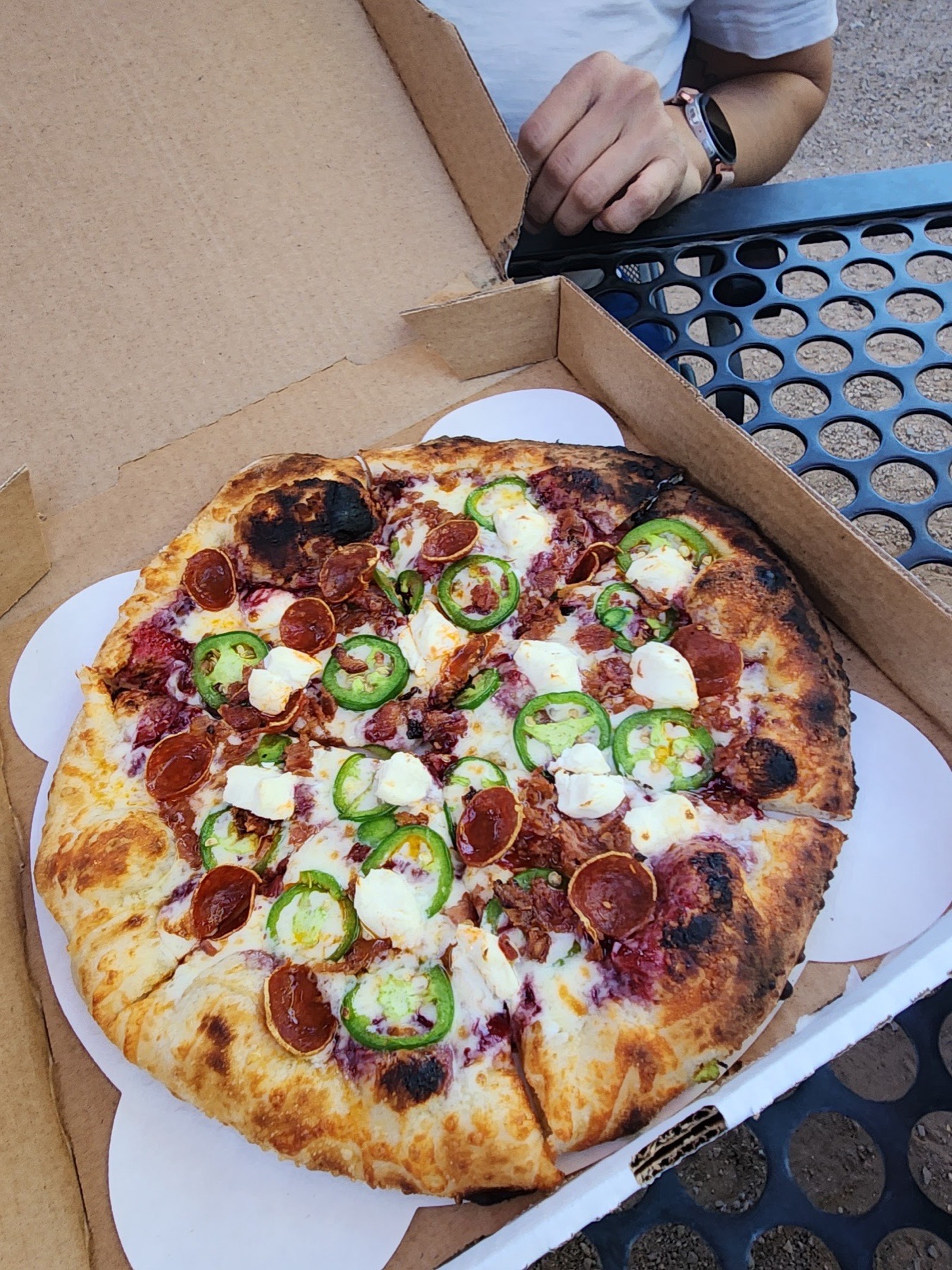 A wood-fired pizza with pepperoni, jalapeños and dollops of soft cheese in a box.